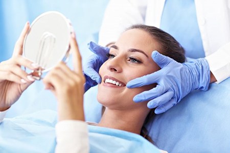woman in dental chair admiring her smile in handheld mirror 