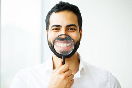 man holding magnifying glass up to his teeth after smile makeover