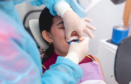 Youth in dental chair with eyes closed as dentist places fluoride trays over her teeth