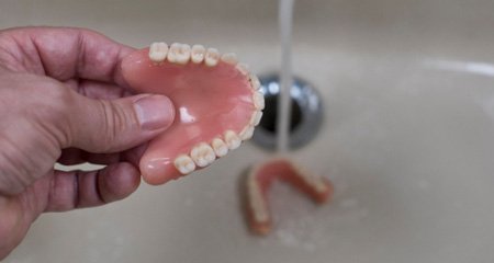 A denture being rinsed with tap water