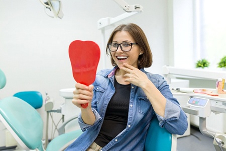 Woman in dental chair smiling into dental mirror