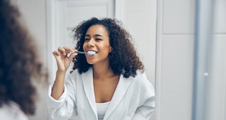 woman brushing her teeth in front of a mirror