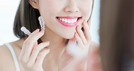 Woman looking at her smile and holding Invisalign orthodontics aligner