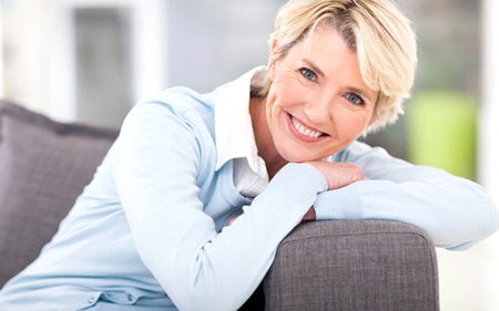 A middle-aged woman leaning against the arm of a couch and smiling after being treated for gum disease in Gainesville