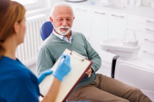 Dental team member holding clipboard and speaking to patient.